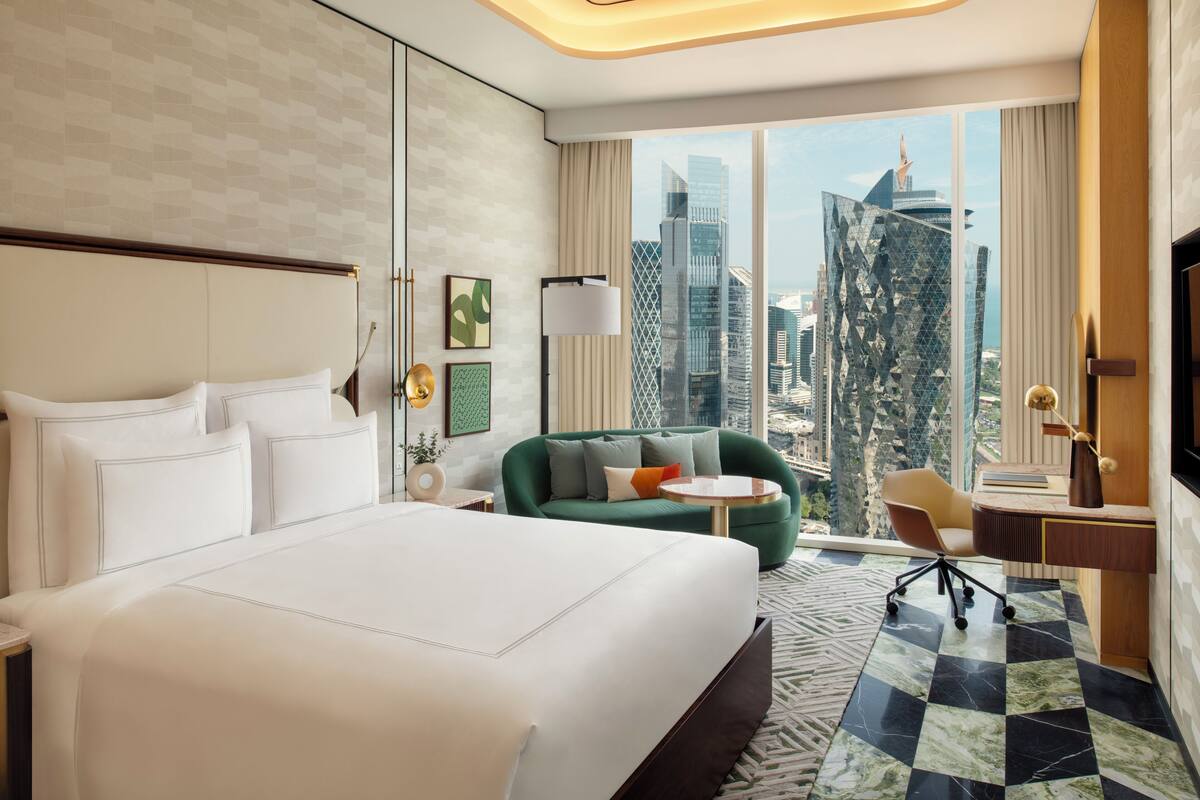 Habitación de hotel con una cama grande, un sofá verde, un escritorio y vistas a la ciudad.