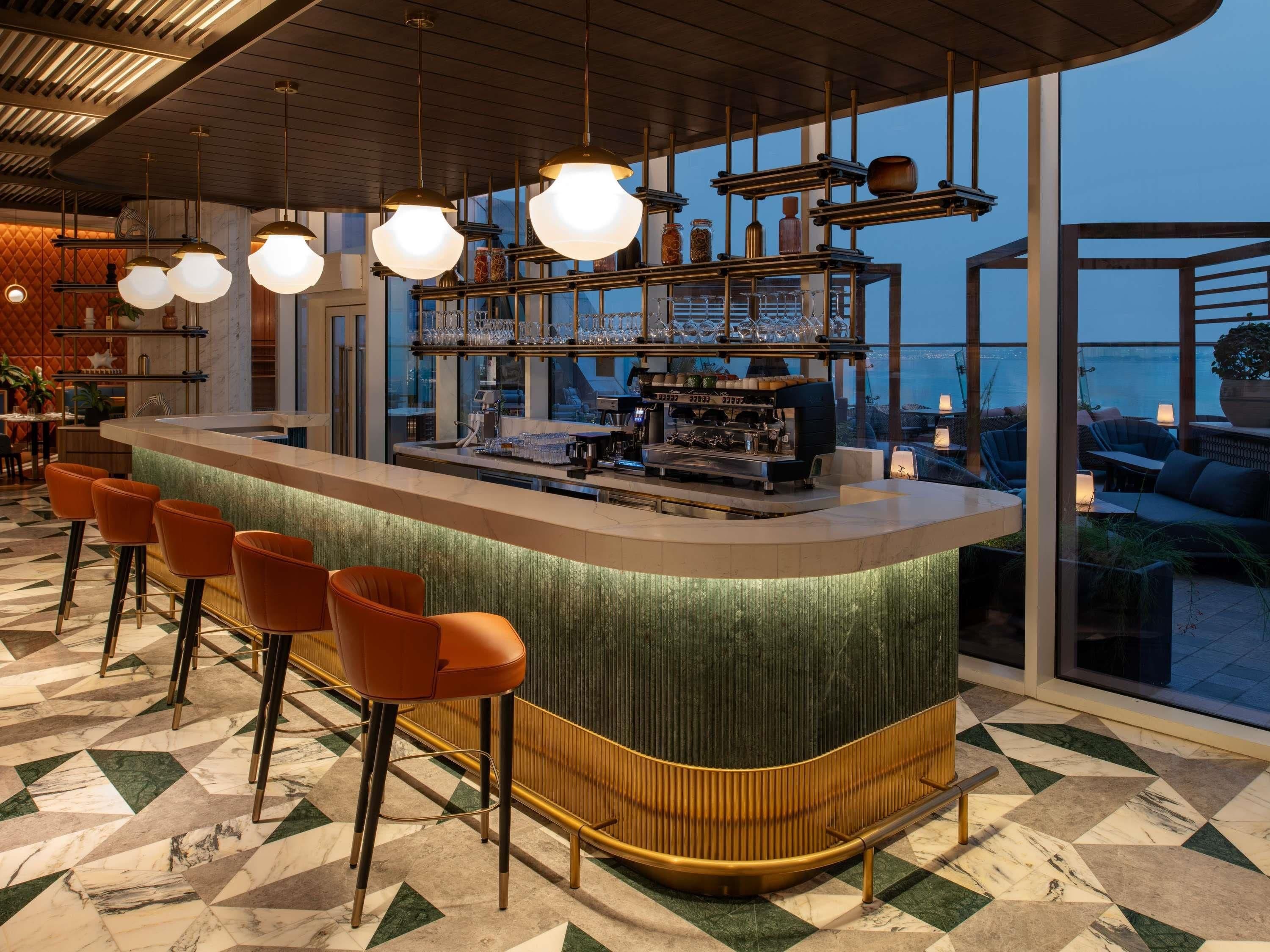 A bar area with a curved counter, bar stools, and a view of the sea through large windows.
