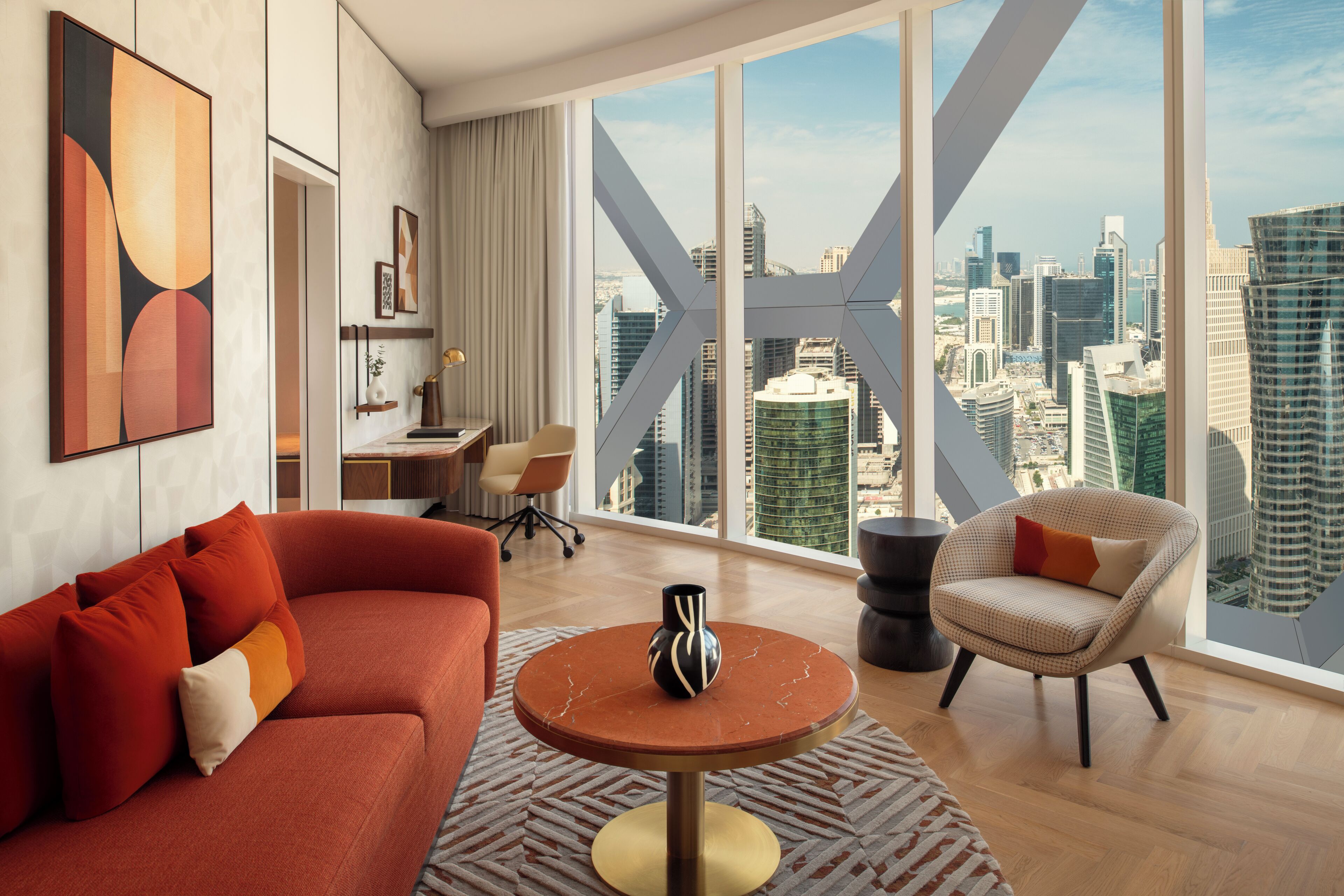 Una sala de estar moderna con un sofá rojo, una mesa de centro redonda y vistas de un paisaje urbano a través de ventanas amplias.