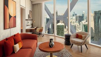 Una sala de estar moderna con un sofá rojo, una mesa de centro redonda y vistas de un paisaje urbano a través de ventanas amplias.
