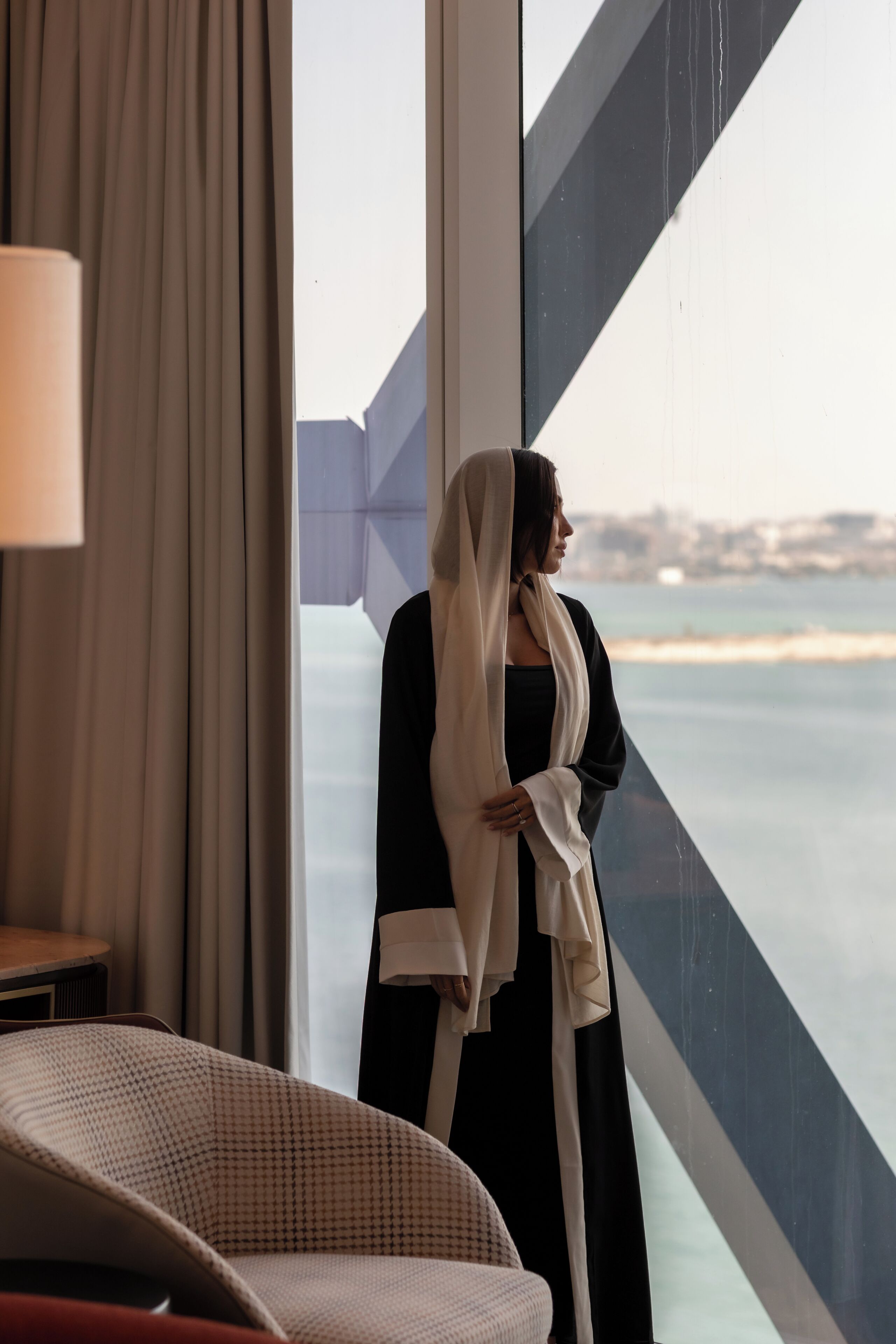 A room with a large window, a chair, and a person standing by the window.