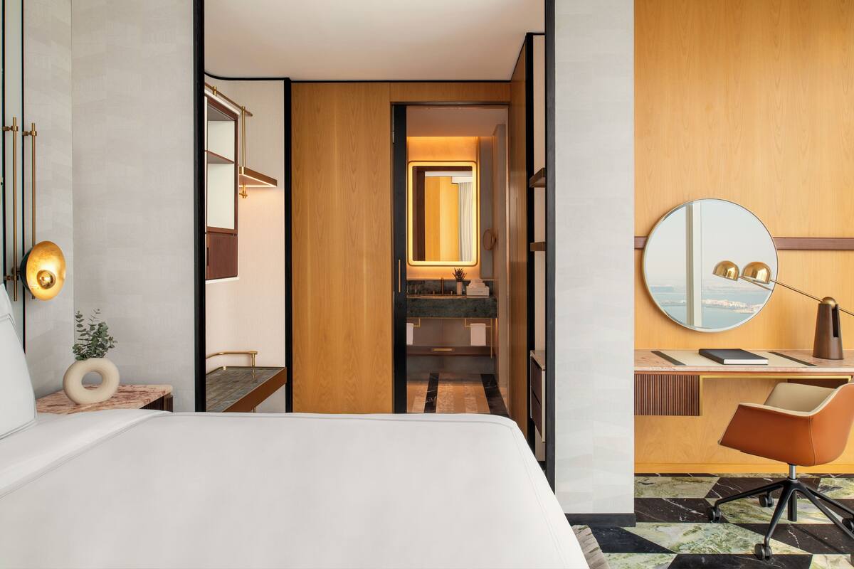 Habitación de hotel con cama, un escritorio con silla, un espejo redondo y vista al mar por la ventana.