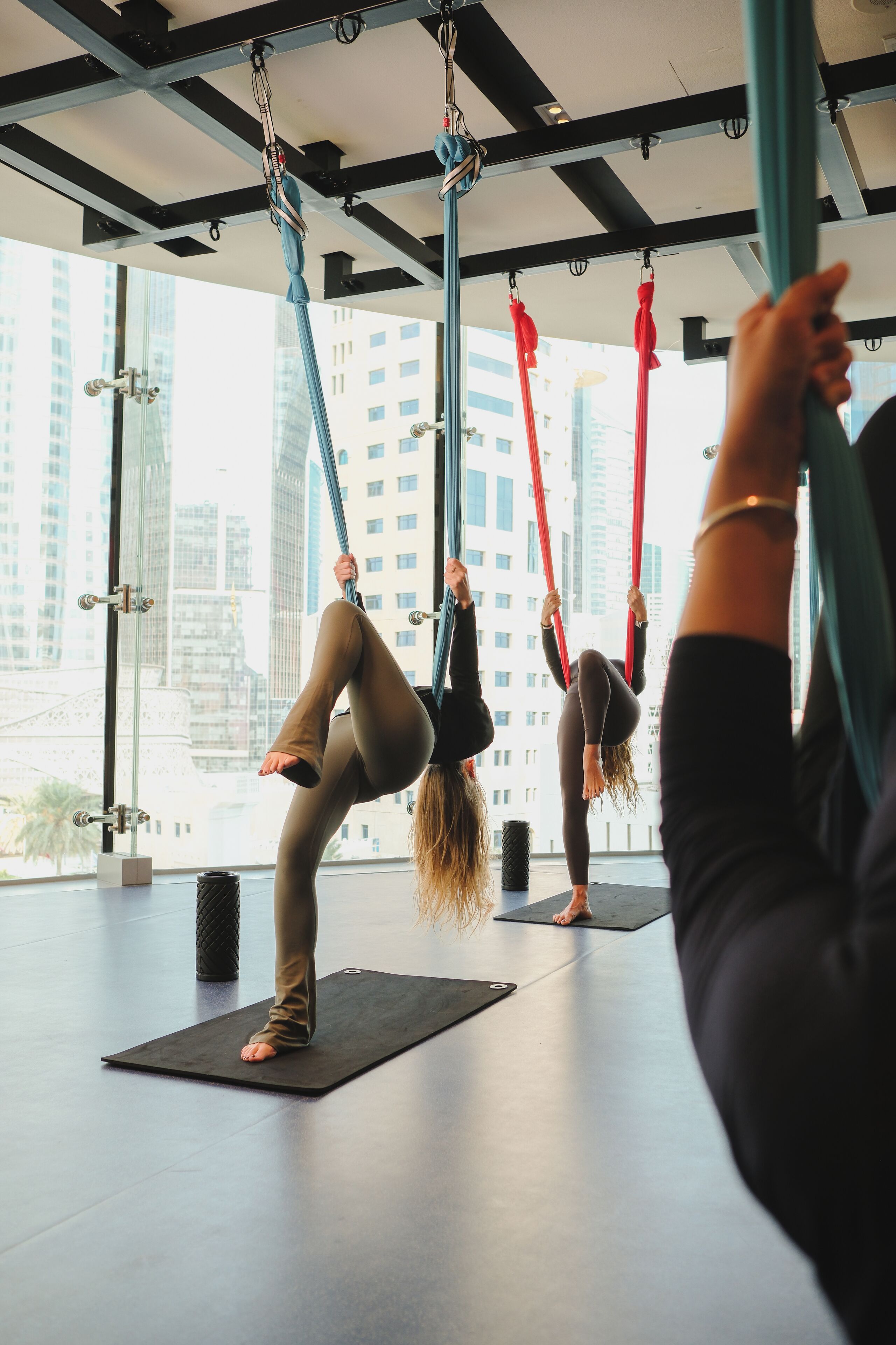 Un studio de yoga équipé de voiles aériennes, doté de grandes fenêtres et offrant une vue sur le paysage urbain.