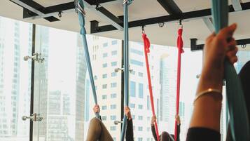 Un estudio de yoga con sedas aéreas, ventanas amplias y vista a un paisaje urbano.