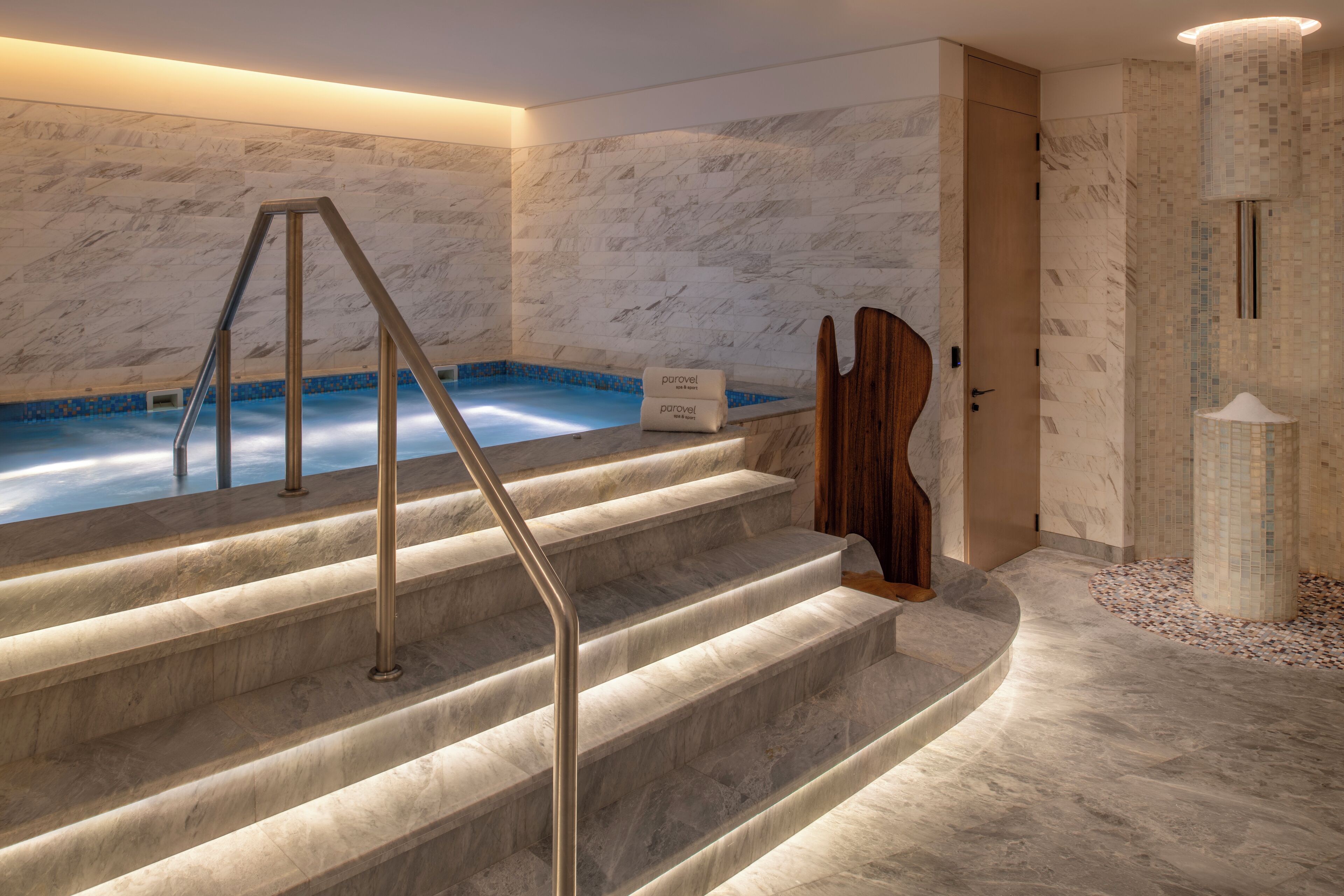 A spa area with a marble staircase leading to a hot tub, a wooden door, and a tiled wall.