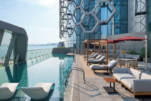 Une piscine à débordement située sur le toit, avec des chaises longues et des parasols, offrant une vue panoramique sur la ville.