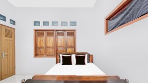 Un dormitorio con una cama de madera, un armario, un ventanal con contraventanas y un tragaluz.