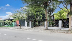 Una calle pavimentada con una entrada porticada, árboles y edificios al fondo.