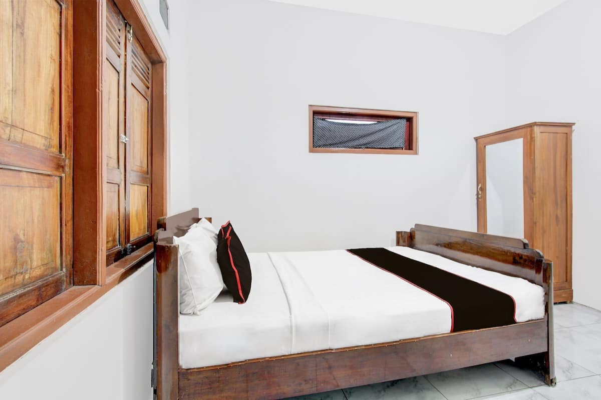 Ein Schlafzimmer mit einem hölzernen Bett, weißer Bettwäsche, einem Holzschrank und einem Fenster mit einem gemusterten Rollo.