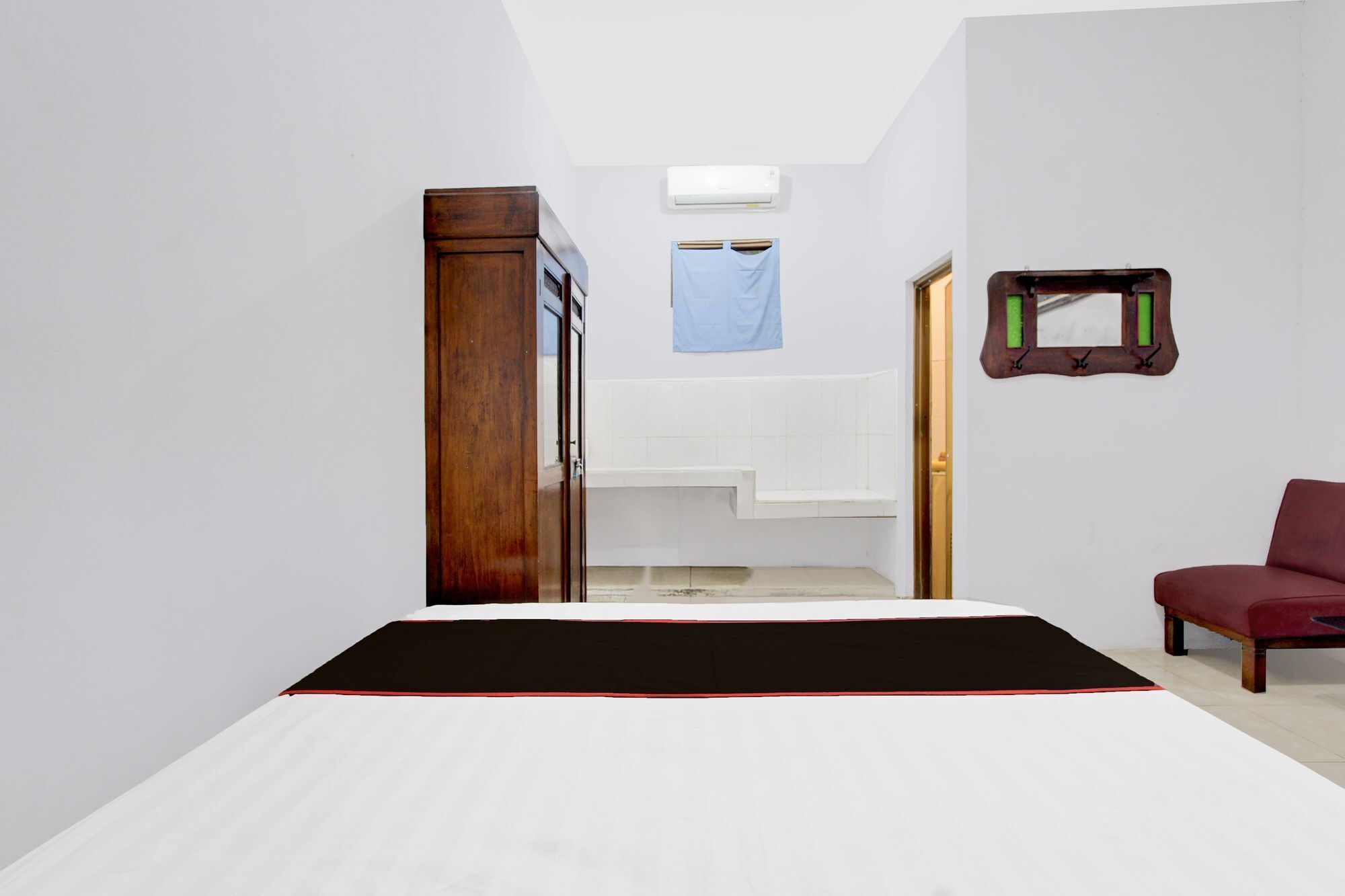A bedroom with a bed, a wooden wardrobe, a mirror, and a red chair.