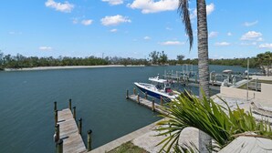 A marina with a docked boat, a palm tree, and a view of the water and distant shoreline. - Oasis by the water. (Sarasota)
