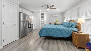 A bedroom with a bed, a nightstand, a ceiling fan, and a view of the kitchen. - Oasis by the water. (Sarasota)