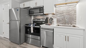 A modern kitchen with stainless steel appliances, white cabinetry, and a brick-pattern backsplash. - Oasis by the water. (Sarasota)