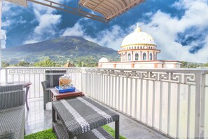 A balcony with wicker furniture and a table with snacks, overlooking a mountainous landscape and a white-domed building. - Hotel O Guesthouse Sabar Makmur Kledung (Kledung)
