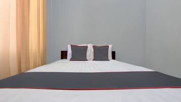 Ein ordentlich bezogenes Bett mit weißer und grauer Bettwäsche, ein dunkelroter Akzent am Fußende und ein Holz-Kopfteil.