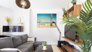 A modern living room with a grey sofa, a black coffee table with a plant, a wooden TV stand, and a painting of a beach scene. - Tenohomes Ocean Light (Buenavista del Norte)