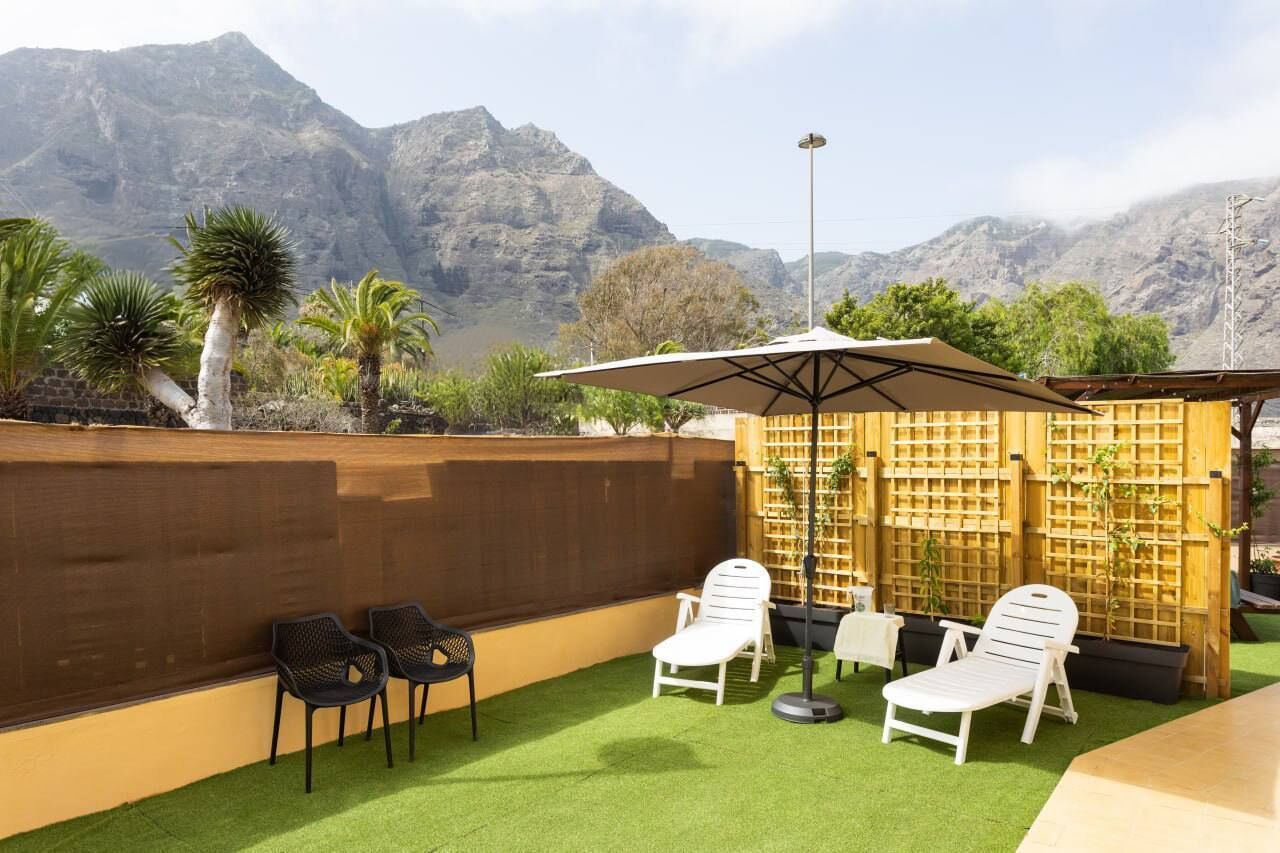 A patio with white lounge chairs, a wooden fence, and a view of mountains.