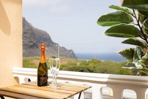 Uma garrafa de vinho Cinzano e um copo sobre uma mesa de madeira, com vista para uma paisagem montanhosa.