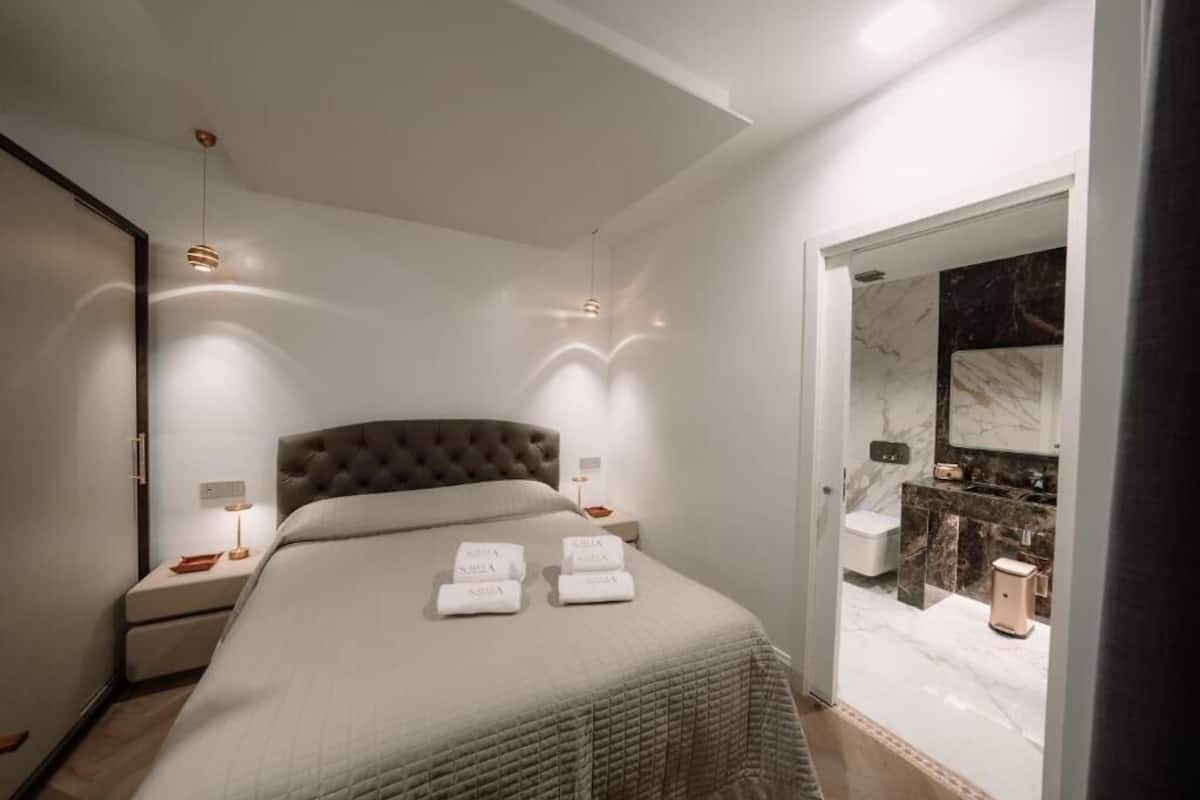 Une chambre moderne avec un grand lit, des tables de chevet et une salle de bain visible à travers une porte ouverte.