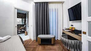 Une chambre d’hôtel moderne équipée d’un lit, d’un petit coin salon, d’une télévision et d’une salle de bain visible à travers une porte ouverte.