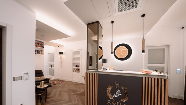 Un espace d’accueil au design moderne, avec un comptoir noir orné du logo « SOFIA Ultra Suite Collection ». Des luminaires suspendus sont placés au-dessus du comptoir, et un grand miroir reflète l’ensemble de la pièce.