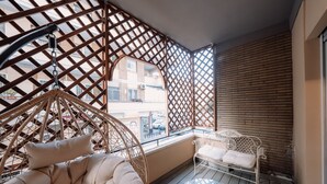Un balcon agrémenté de meubles en osier, d’une table en verre et offrant une vue sur les immeubles.