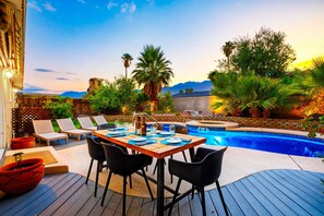 A poolside area with a wooden deck, lounge chairs, a dining table set for two, and a hot tub. - 25% Off Aug! Perfect For Families -Pool, Jacuzzi* (Palm Springs)