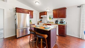 A modern kitchen with wooden cabinets, a stainless steel refrigerator, a granite countertop, and a bar stool area. - 30% Off September Perfect 4 Families Pool, Jacuzzi (Palm Springs)