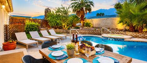 A poolside dining area with a table set for two, lounge chairs, and a pool.