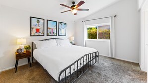 A bedroom with a bed, a nightstand with a lamp, a ceiling fan, and framed pictures on the wall. - 30% Off September Perfect 4 Families Pool, Jacuzzi (Palm Springs)