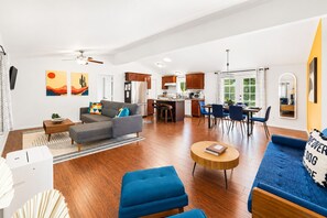 A modern living room with a sofa, ottoman, and coffee table. There is a kitchen area with a dining table and chairs.