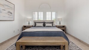 A bedroom with a bed, two bedside tables, a bench, a ceiling fan, and a window with shutters. - Scottsdale Escape: Expansive, Stylish 3-Bedroom (Scottsdale)