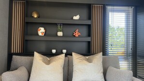 En moderne stue med en grå sofa, pynteting på hylder og et vindue med rullegardiner.
