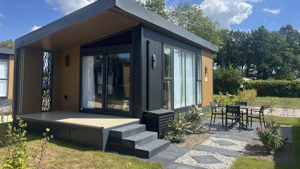 Et moderne hus med en overdækket veranda, store skydedøre og en terrasse med udendørs møbler.