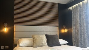 Et hotelværelse med moderne design, der indeholder en stor seng med mange puder, en sengegavl med vandrette lister og to vægmonterede lamper.