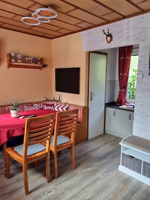 A dining area with a wooden table and chairs, a wall-mounted shelf with dishes, a mounted deer head, and a door leading to a kitchen.