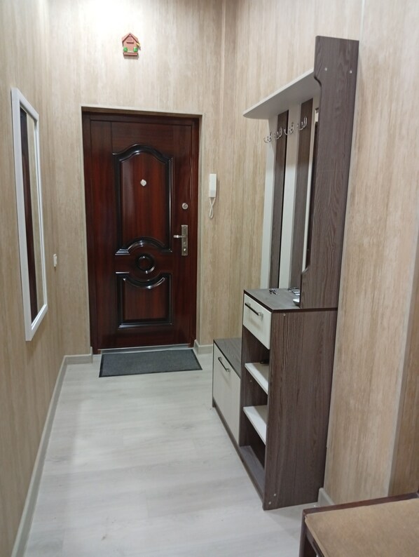 A hallway with a wooden door, a small shelf, and a wall-mounted telephone.