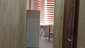 A narrow hallway with a wooden door on the right, a white air conditioning unit on the wall, and a white refrigerator in the center.