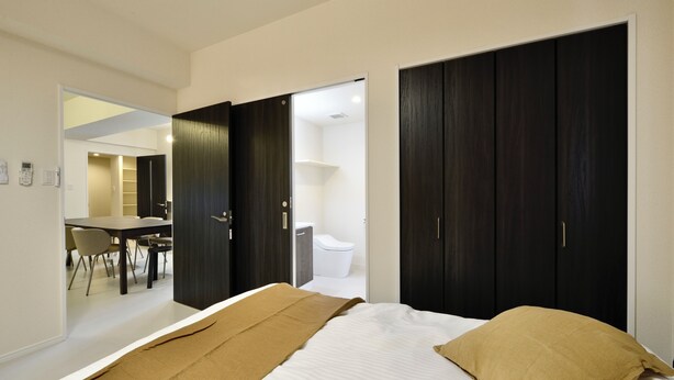 A modern bedroom with a bed, a desk, and a chair in the adjacent room. - Riverside Chibana (Okinawa)