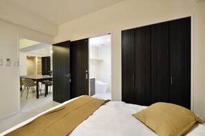 A modern bedroom with a bed, a desk, and a chair in the adjacent room. - Riverside Chibana (Okinawa)