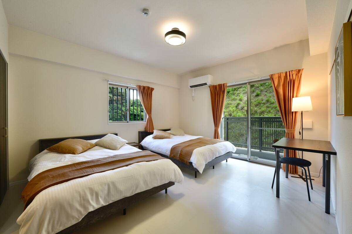 A hotel room with two beds, a desk, and a balcony with curtains.