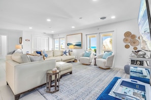 A spacious living room with a white sofa, armchairs, a coffee table, and a large TV. - Island Hoppers - Across From The Beach, Renovated, Pet Friendly! (St. George Island)