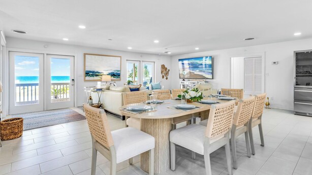 A spacious dining area with a large table, wicker chairs, and a view of the ocean through glass doors.