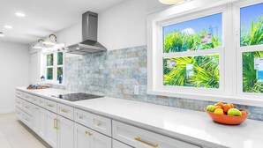 A modern kitchen with white cabinets, a black stove, and a window with a tropical view.