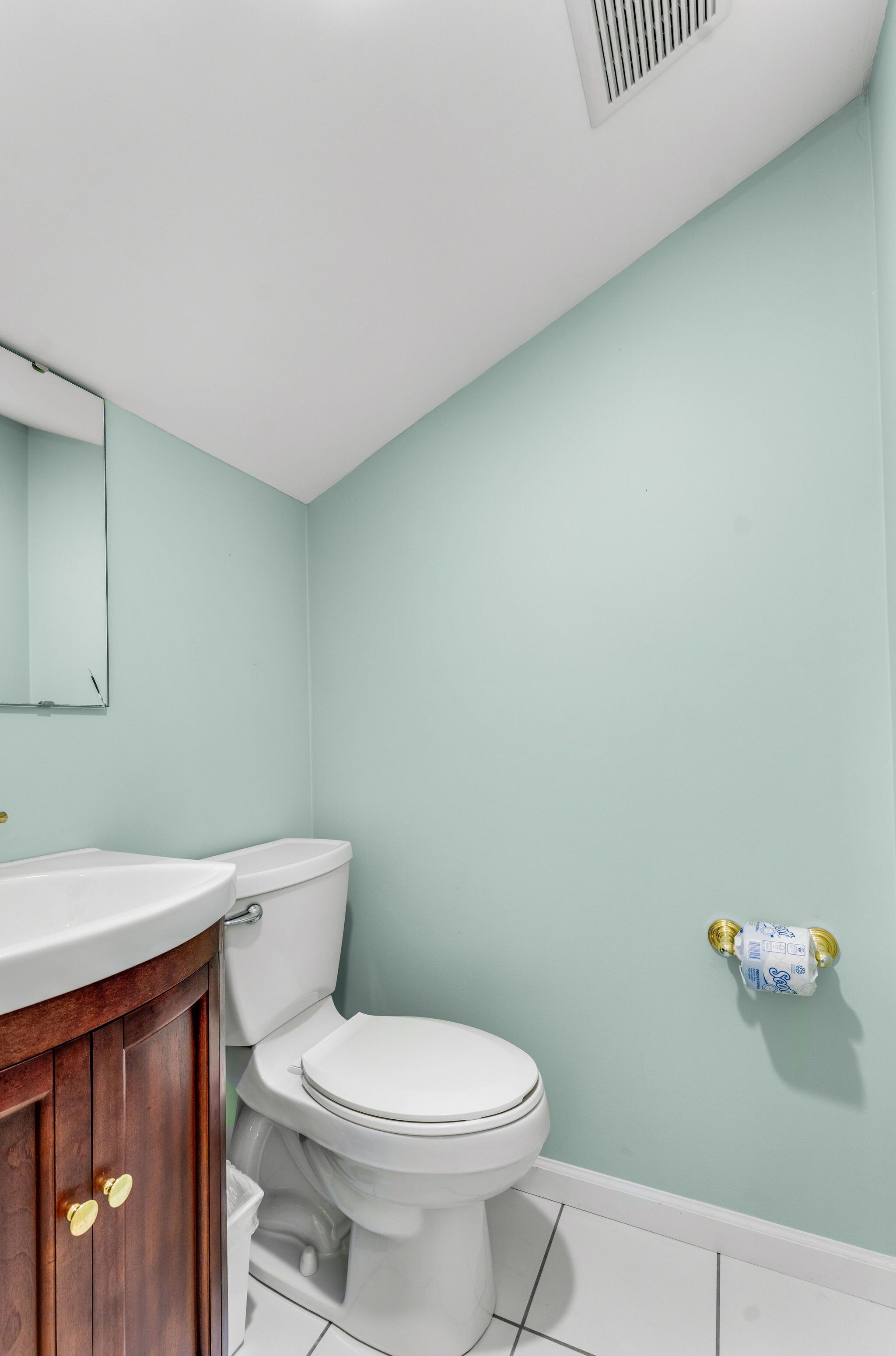 A bathroom with a white toilet, a wooden vanity with gold handles, and a light green wall.