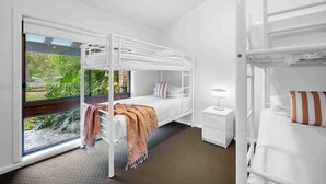 Habitación con literas, una mesita de noche con lámpara, y vista a zonas verdes.