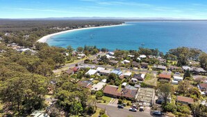 Vista aérea de una zona residencial costera con casas, una playa y barcos en el agua.