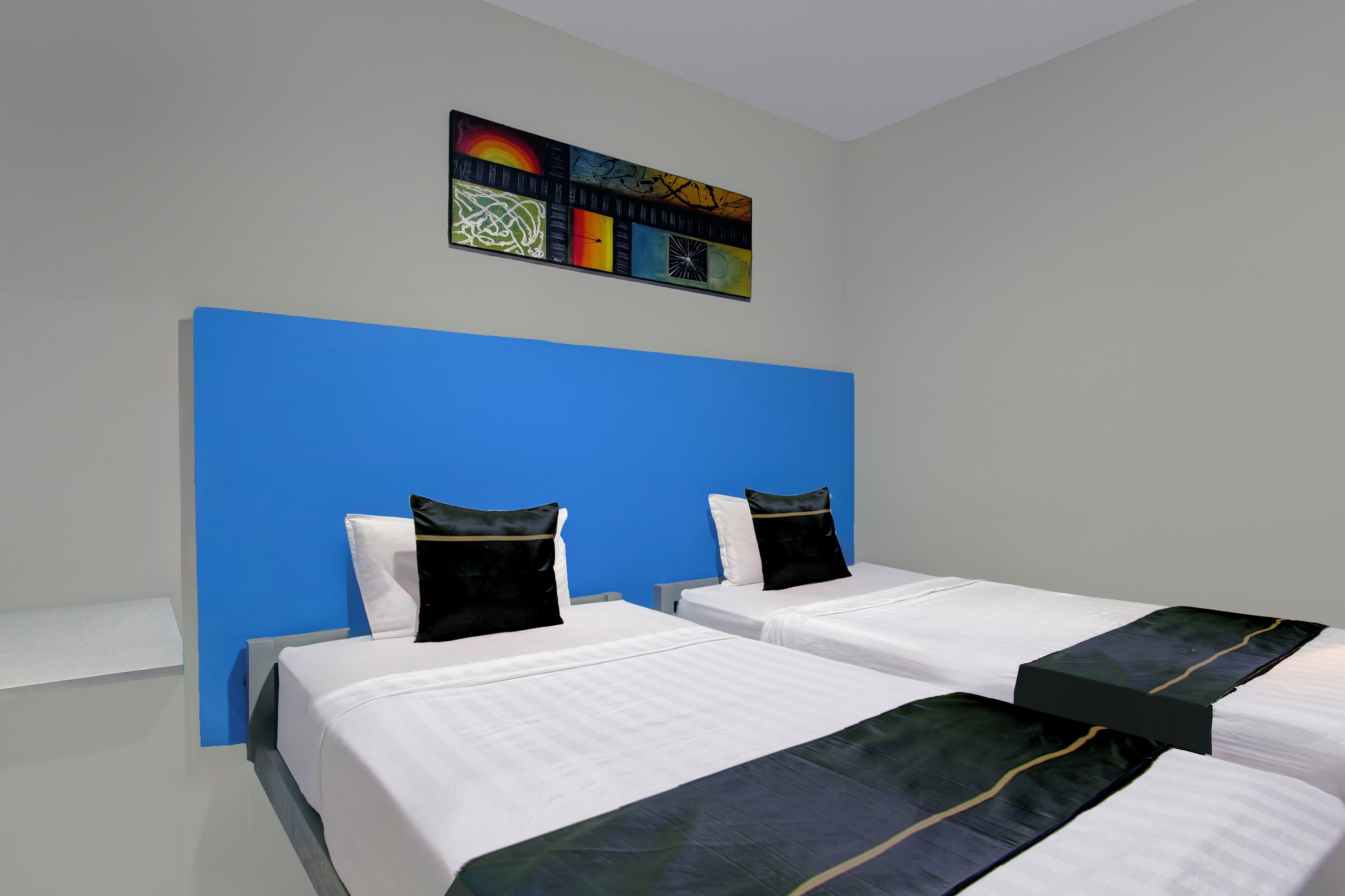 Ein Hotelzimmer mit zwei Betten, einer blauen Akzentwand und einem farbenfrohen abstrakten Gemälde über den Betten.