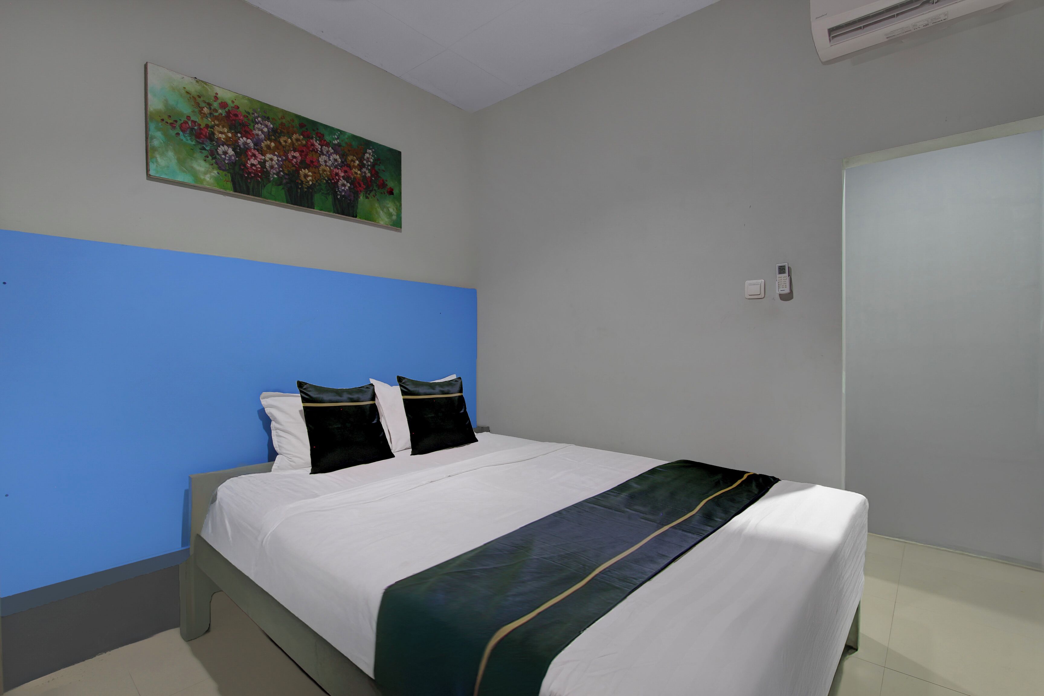 Een hotelkamer met een bed, een schilderij, een lichtschakelaar en een deur.