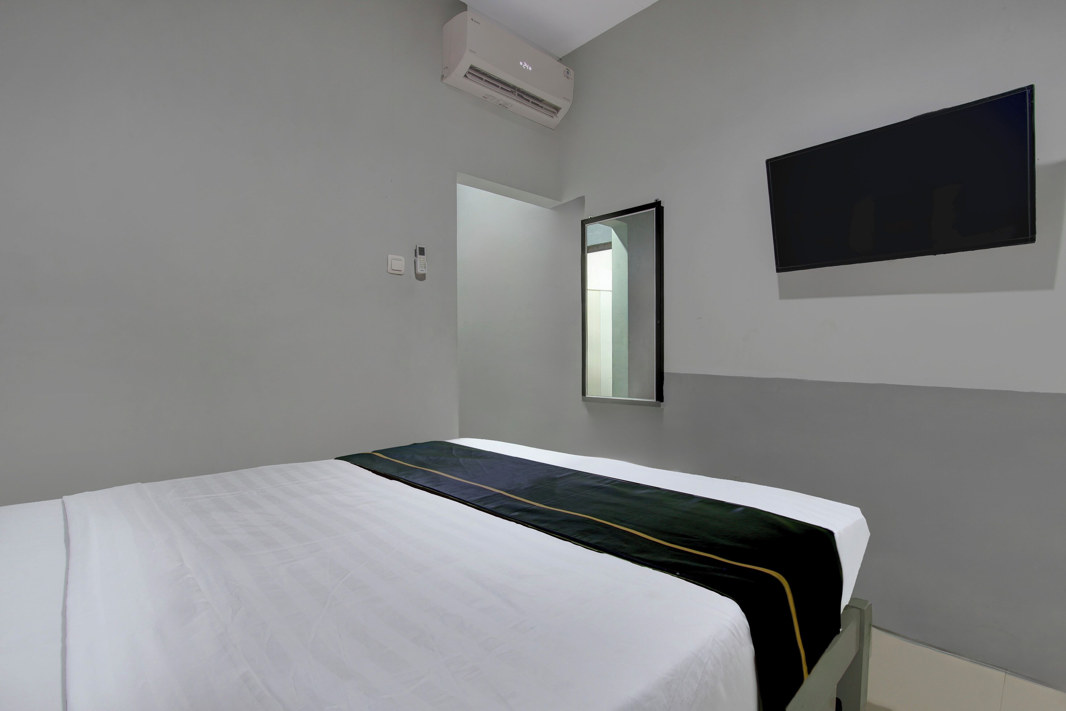 Una habitación con una cama, un televisor de pantalla plana montado en la pared y un equipo de aire acondicionado sobre la cama.